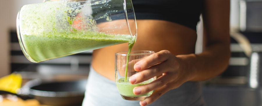 Woman in a black tank top pouring herself green, healthy juice.
