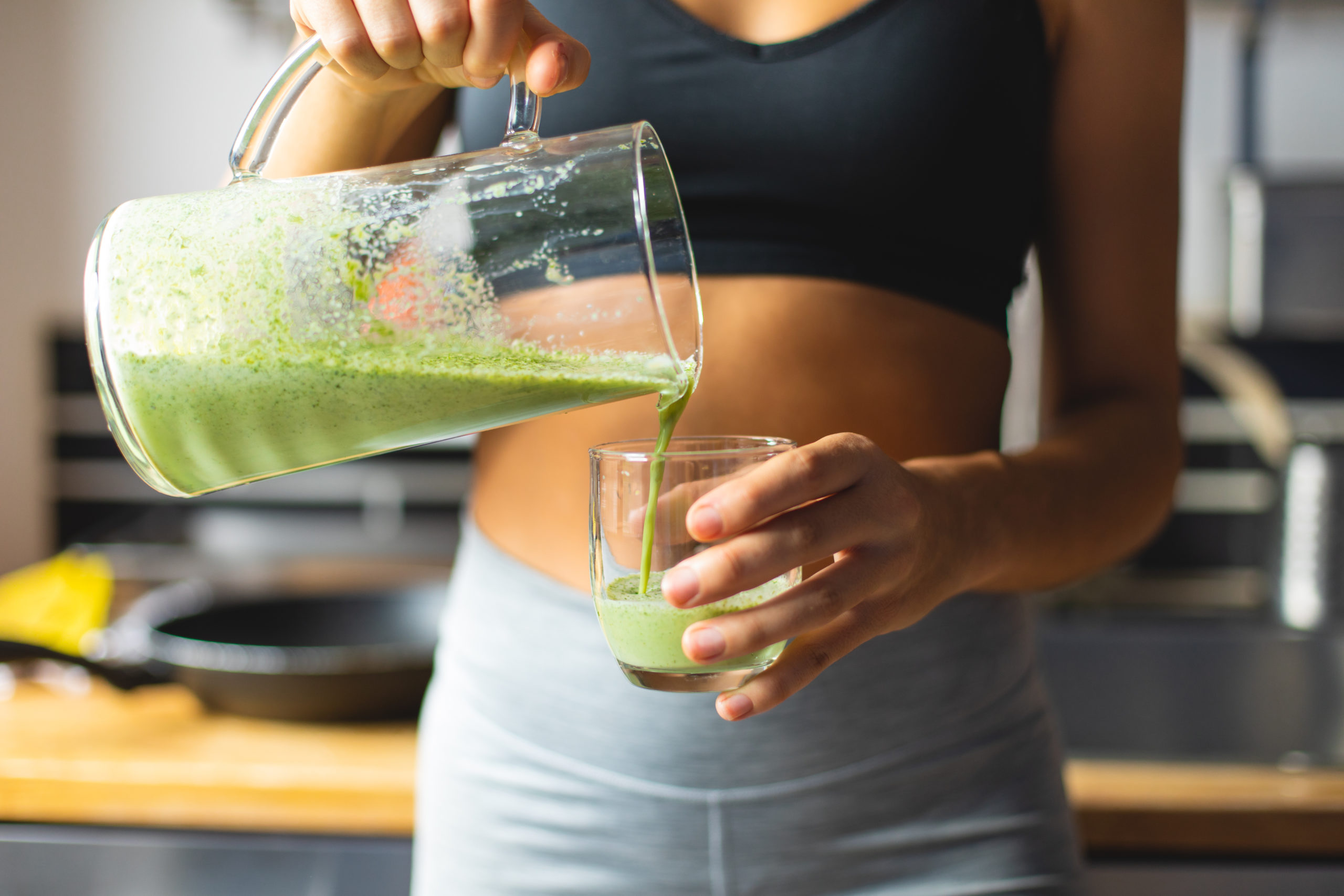Woman in a black tank top pouring herself green, healthy juice.