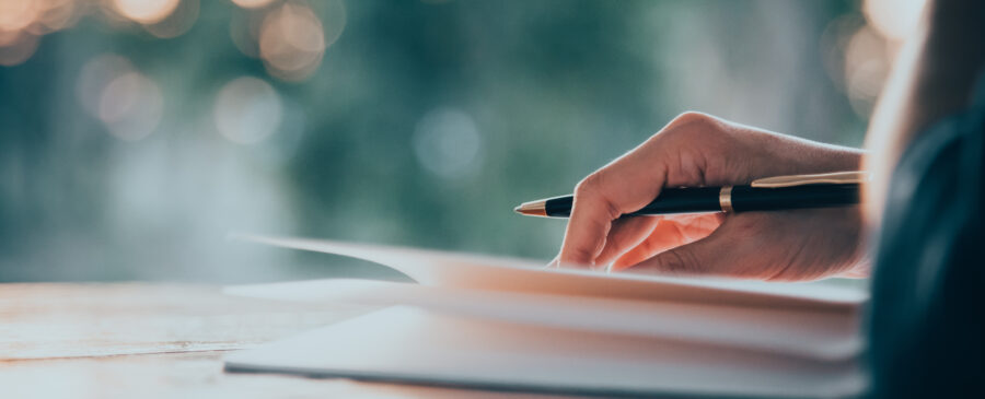 Closeup image of person holding a pen atop a notebook.