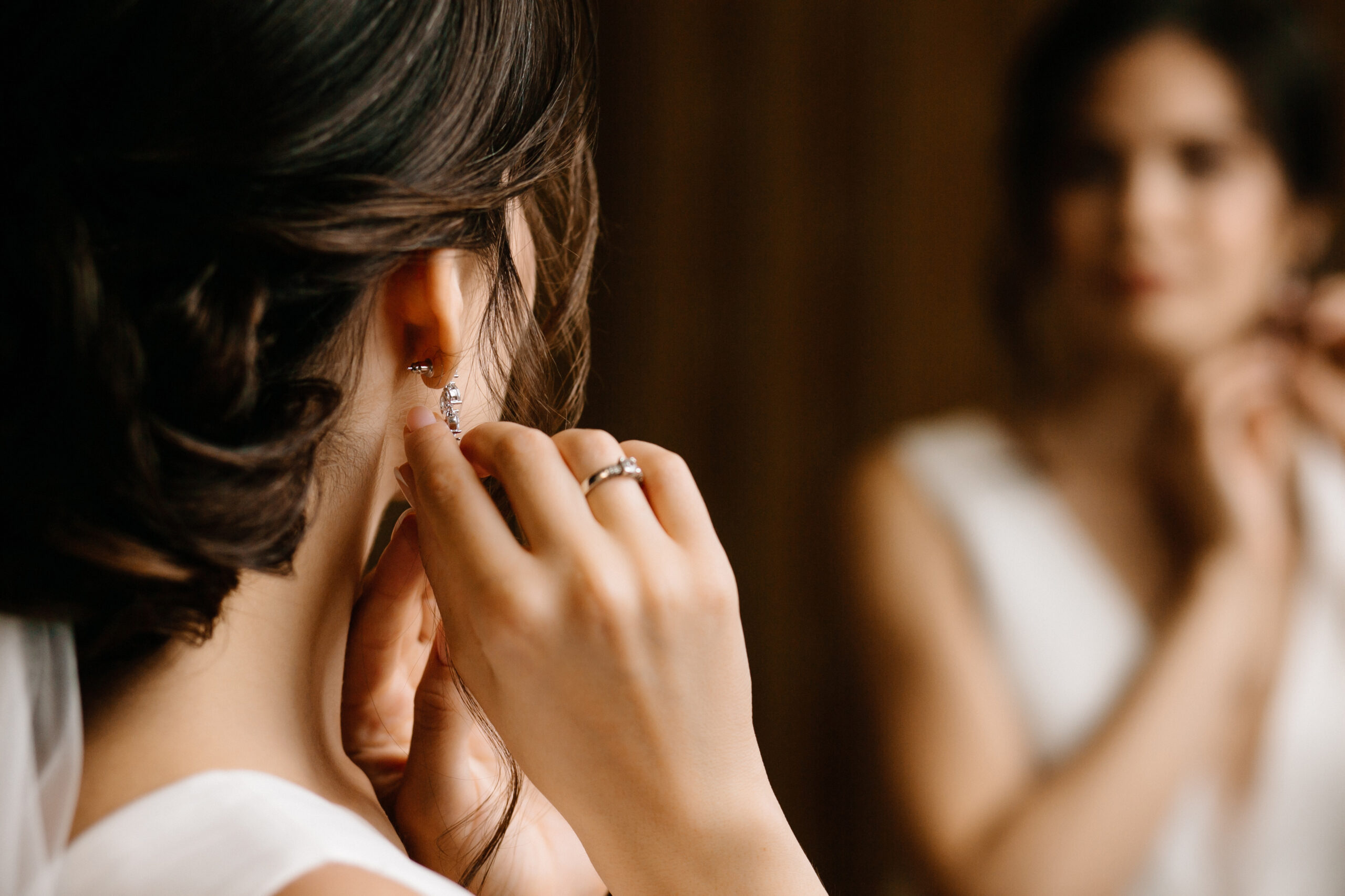 Stunning woman adjusting earrings in front of a mirror.